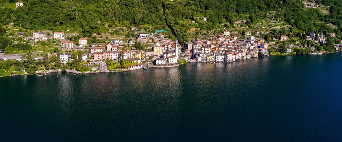 A lakeside town with buildings along the shore and a forested hillside in the background.