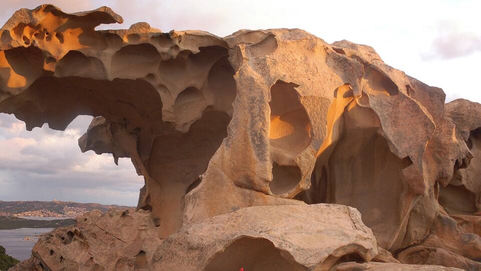 A large rock formation with multiple caves and a coastal landscape in the background.