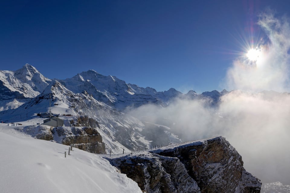 Eine verschneite Berglandschaft mit felsigen Vorsprüngen und einem klaren, blauen Himmel.