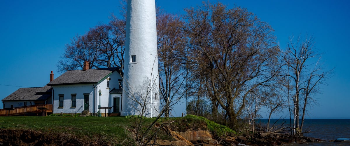 A white lighthouse with a red top, a white building with a green door, and leafless trees.