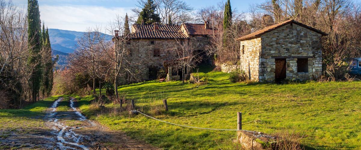 A stone house with a tiled roof, a smaller stone building, and a dirt path leading to the house.
