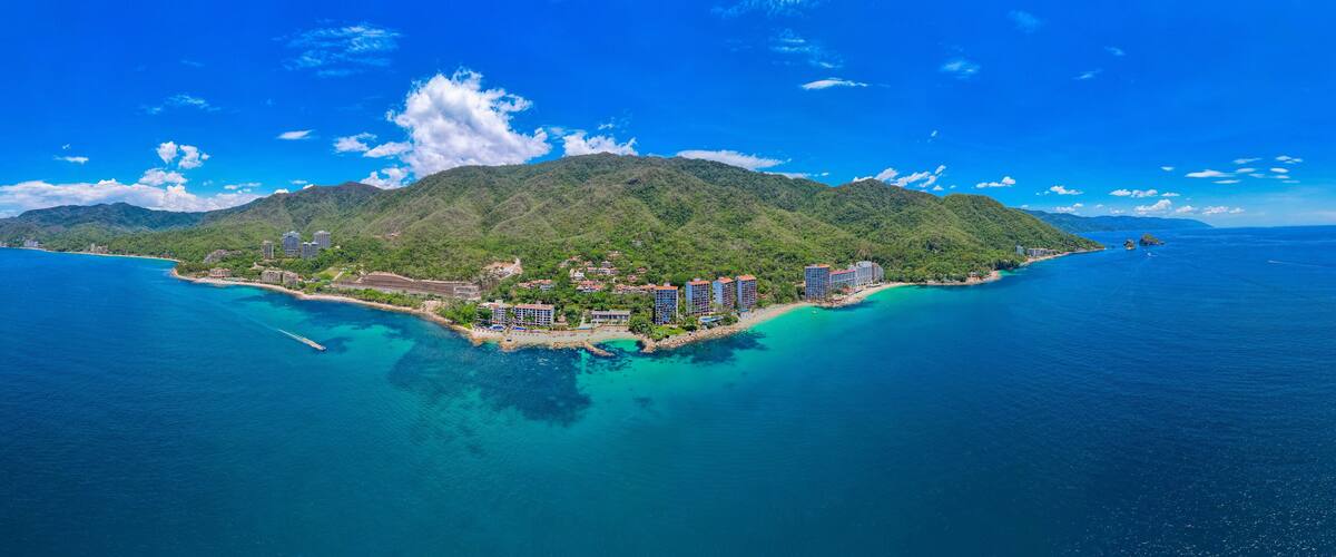 A tropical island with a clear blue sea, lush green mountains, and several high-rise buildings.