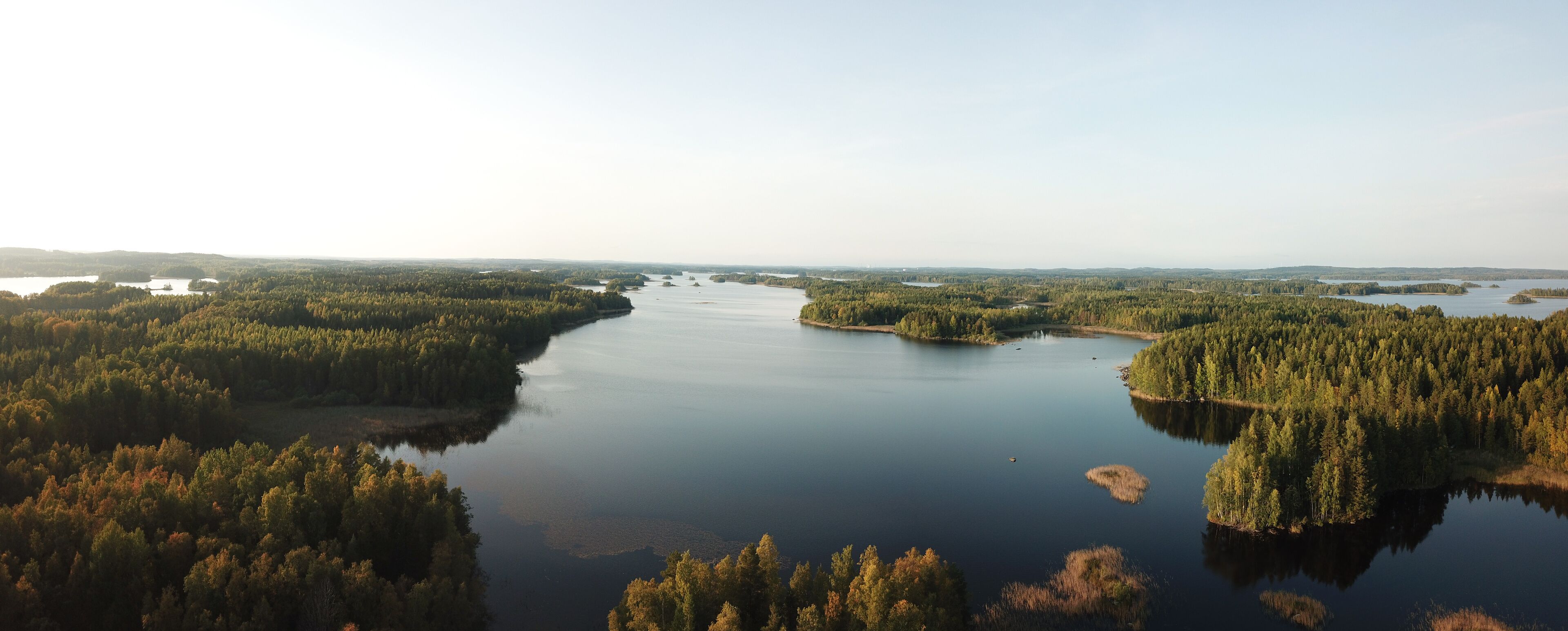 A river winding through a densely forested landscape with several small islands and clear skies.