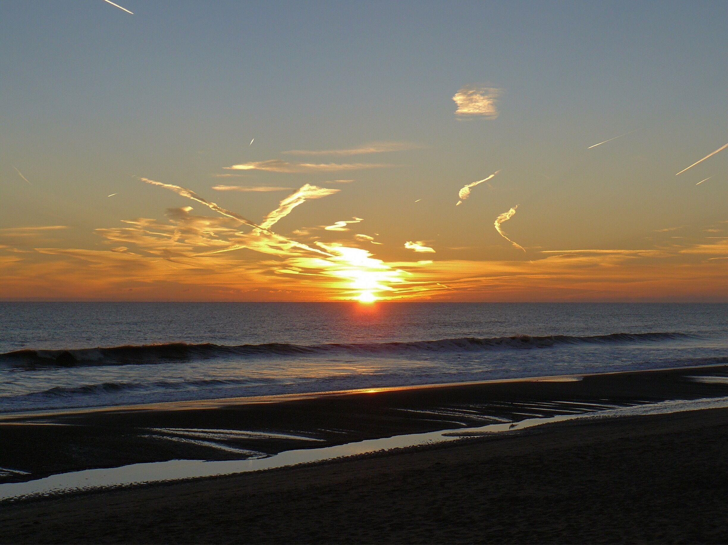 A sunset over the ocean with waves on the shore.