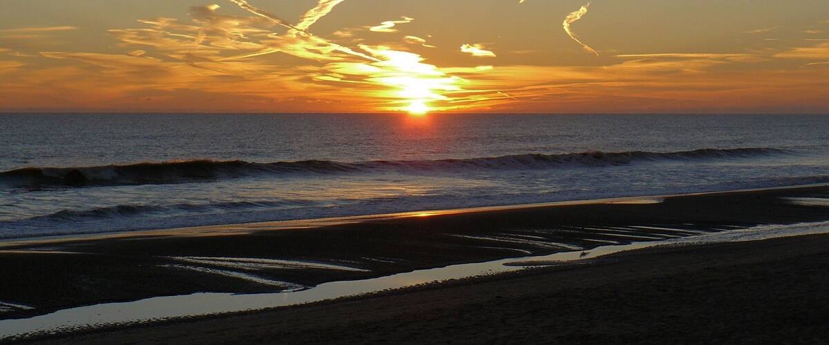 A sunset over the ocean with waves on the shore.