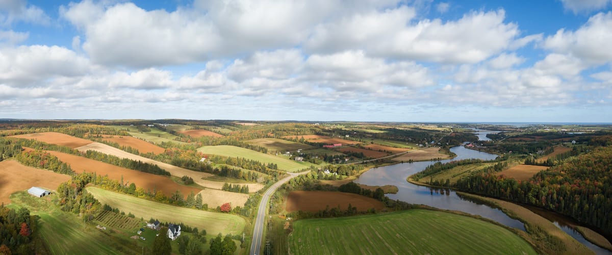 A river winding through rolling farmland with fields in autumn colors, a road, and scattered houses.