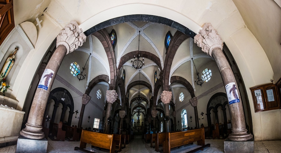 A church interior with high vaulted ceilings, arched windows, and ornate columns.