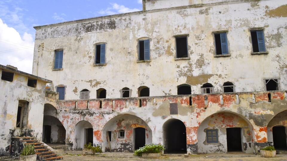 A weathered building with multiple arched doorways and windows, some with shutters.