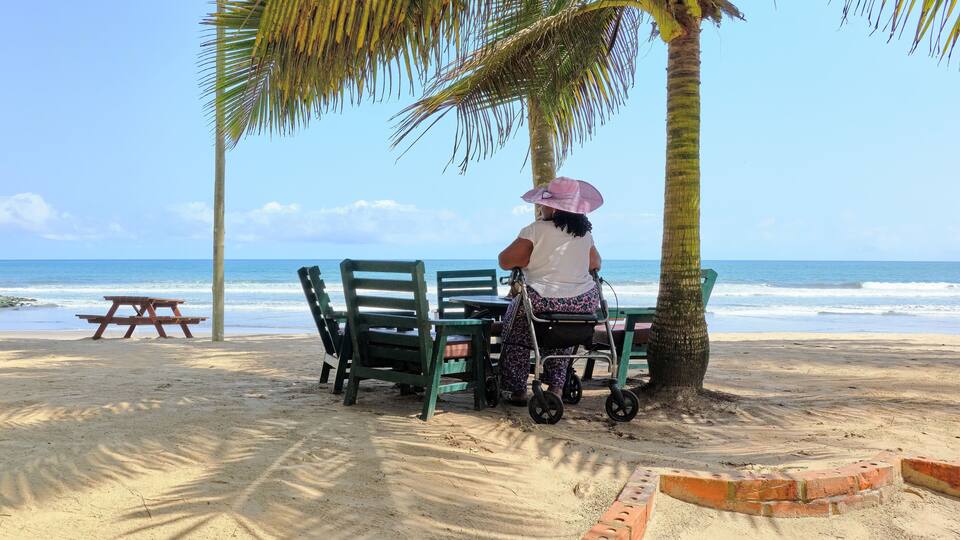 A beach with a woman in a stroller, palm trees, and a wooden picnic table.