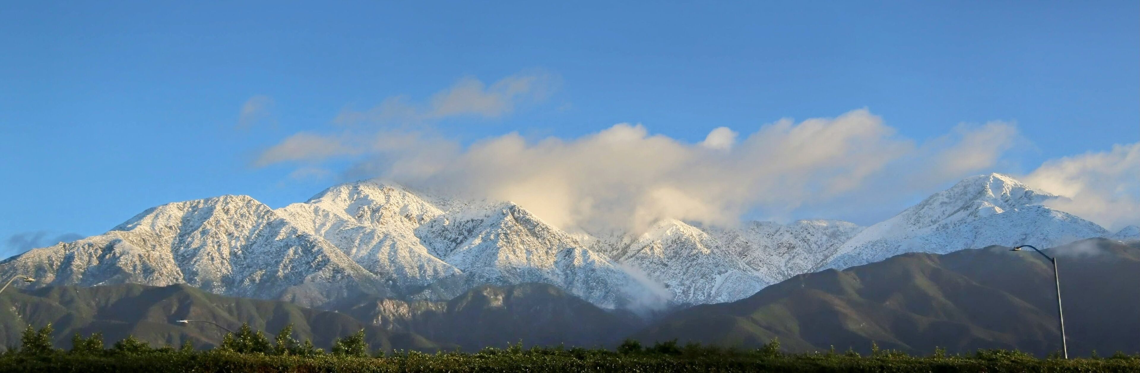 A snow-covered mountain range with a clear sky and a streetlight in the foreground.