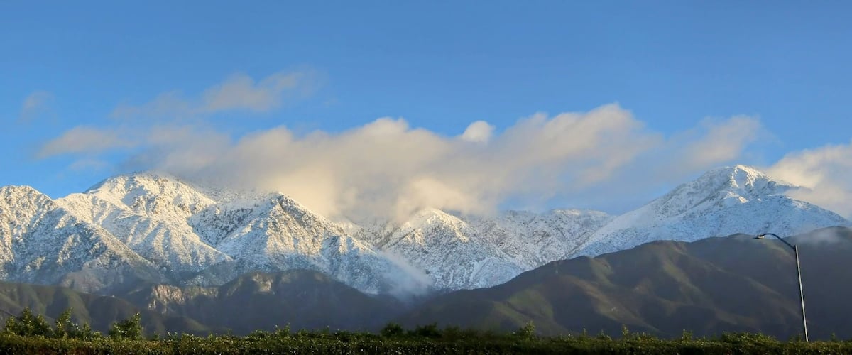 A snow-covered mountain range with a clear sky and a streetlight in the foreground.