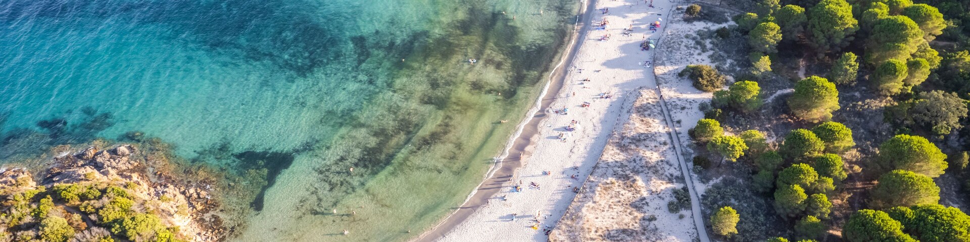 Vista aérea de una playa costera con aguas turquesas cristalinas, orillas de arena y densas selvas verdes.