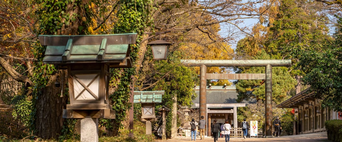 A traditional Japanese torii gate pathway with stone lanterns and a wooden structure in a forested area.
