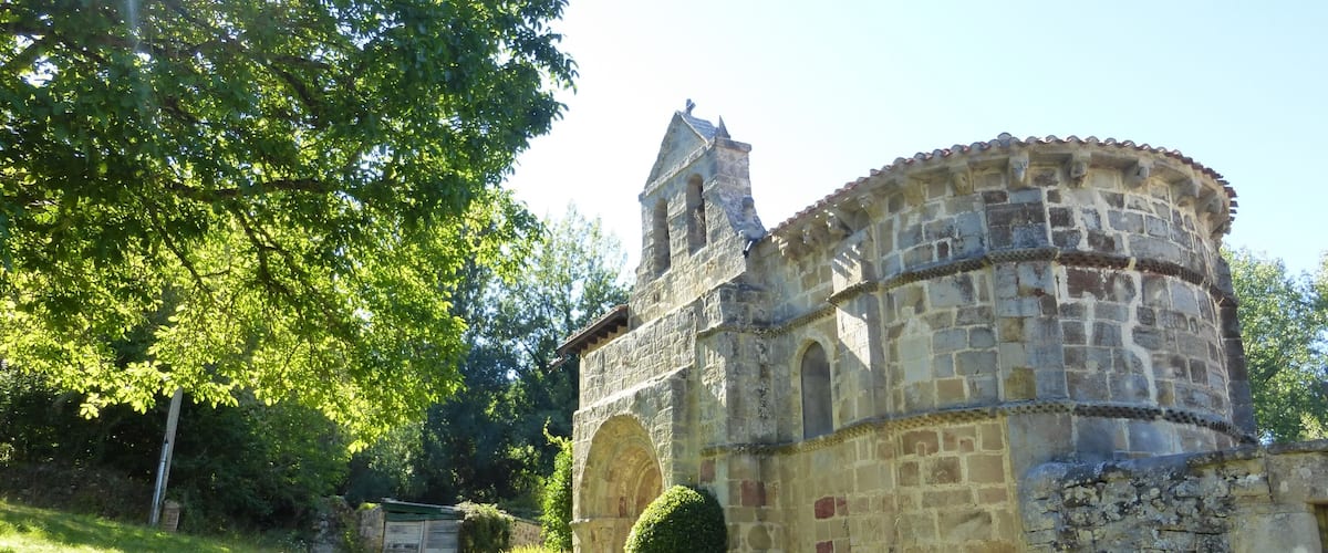 A stone church with a bell tower, surrounded by greenery and a clear sky.