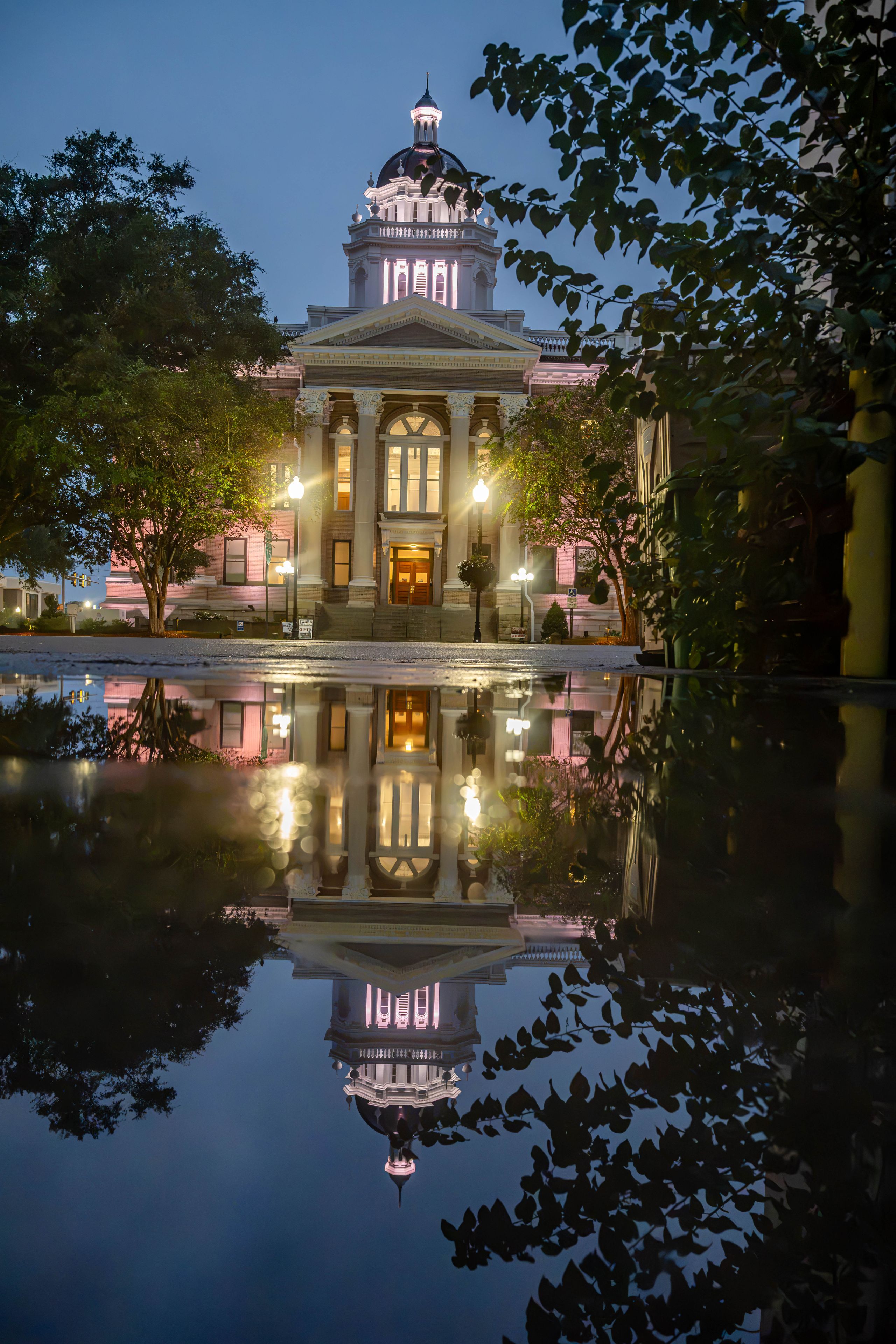 A historic building with a dome and columns, reflected in a calm water body.