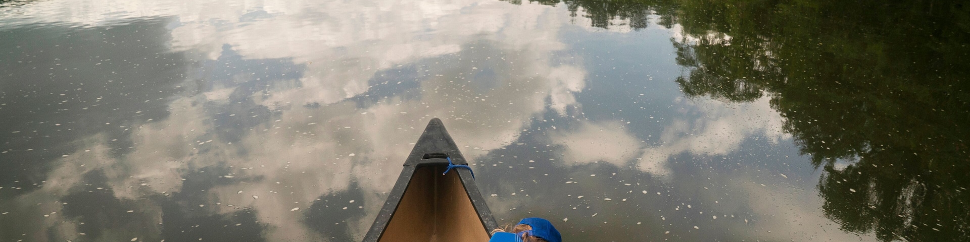 A young girl sits in the bow of a canoe on a slow river