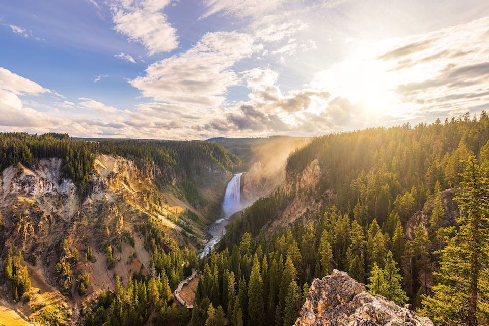 A canyon with a waterfall, dense forest, and rocky terrain.