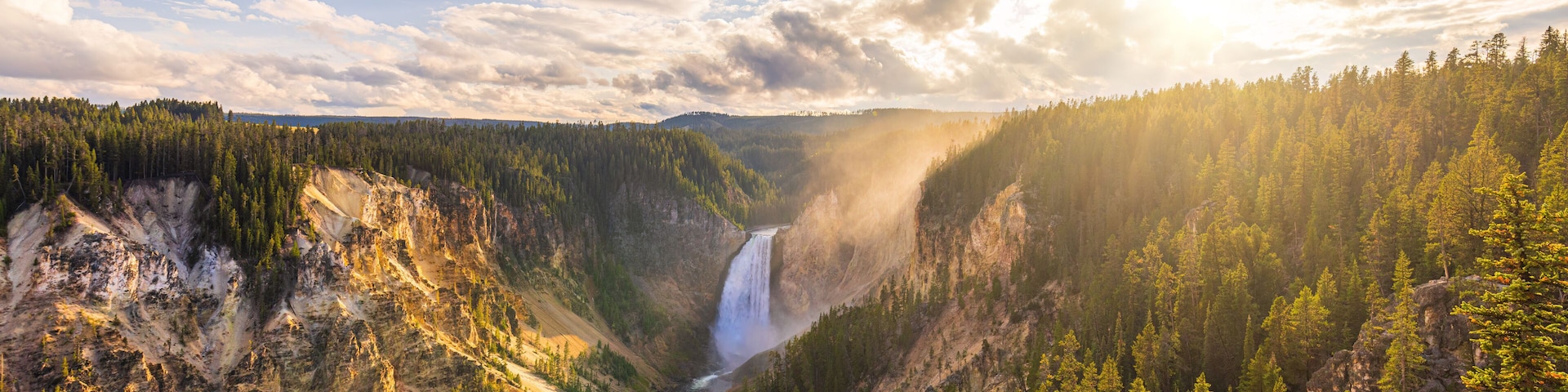 A canyon with a waterfall, dense forest, and rocky terrain.