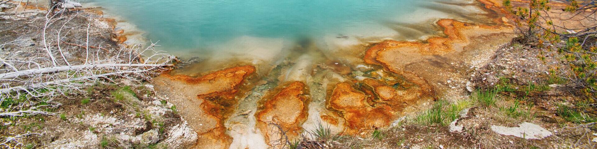 A turquoise lake with mineral deposits, surrounded by forest and hills.