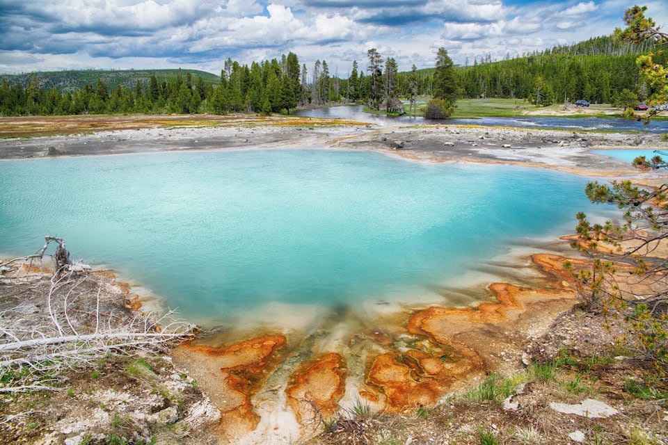Un llac de color turquesa amb dipòsits minerals, envoltat de bosc i turons.