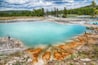 En turkis sø med mineralaflejringer, omgivet af skov og bakker.