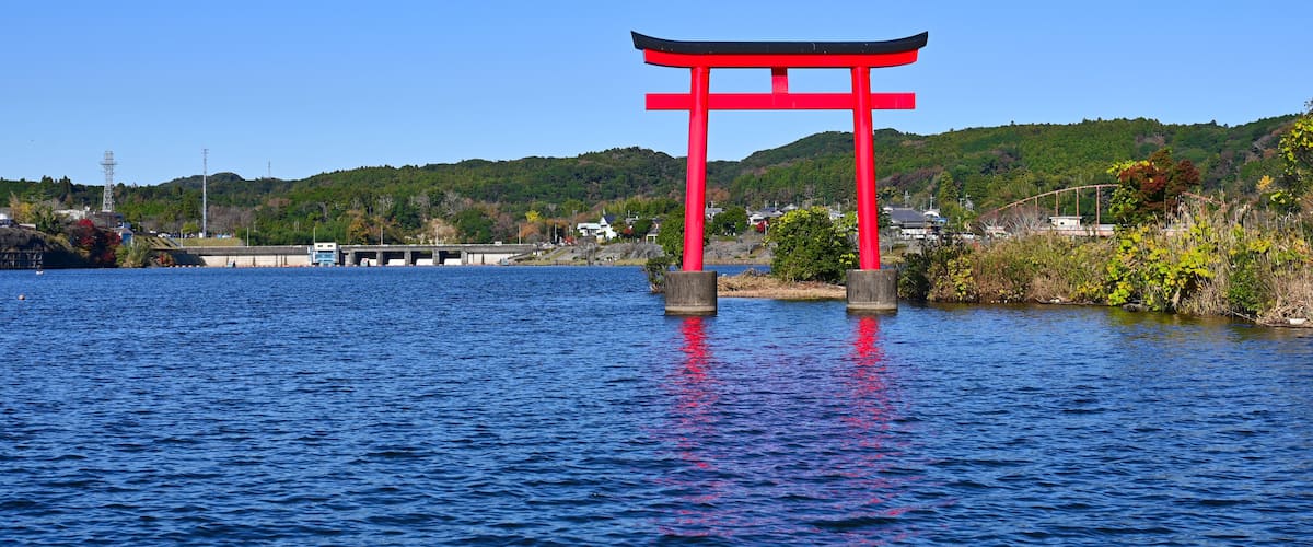A red torii gate in a body of water with a clear blue sky and green hills in the background.