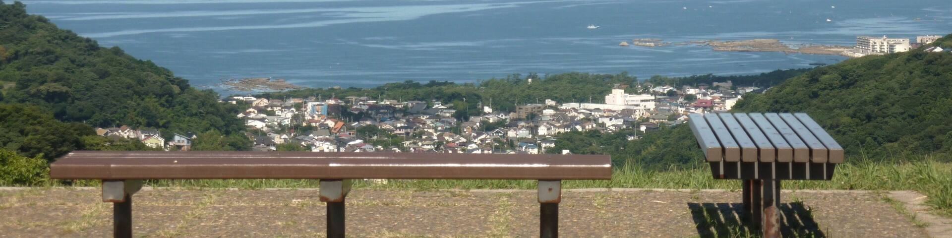 A bench overlooking a coastal town with a mountain in the background.