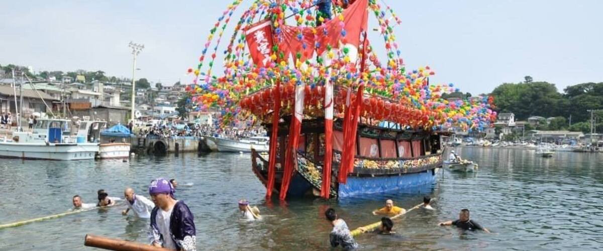 A traditional boat adorned with colorful decorations and a large umbrella, surrounded by people in a body of water.