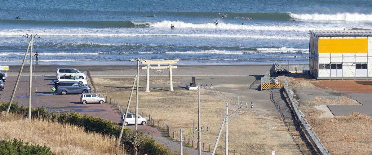 A beach with waves, a parking lot, and a building with a yellow section.