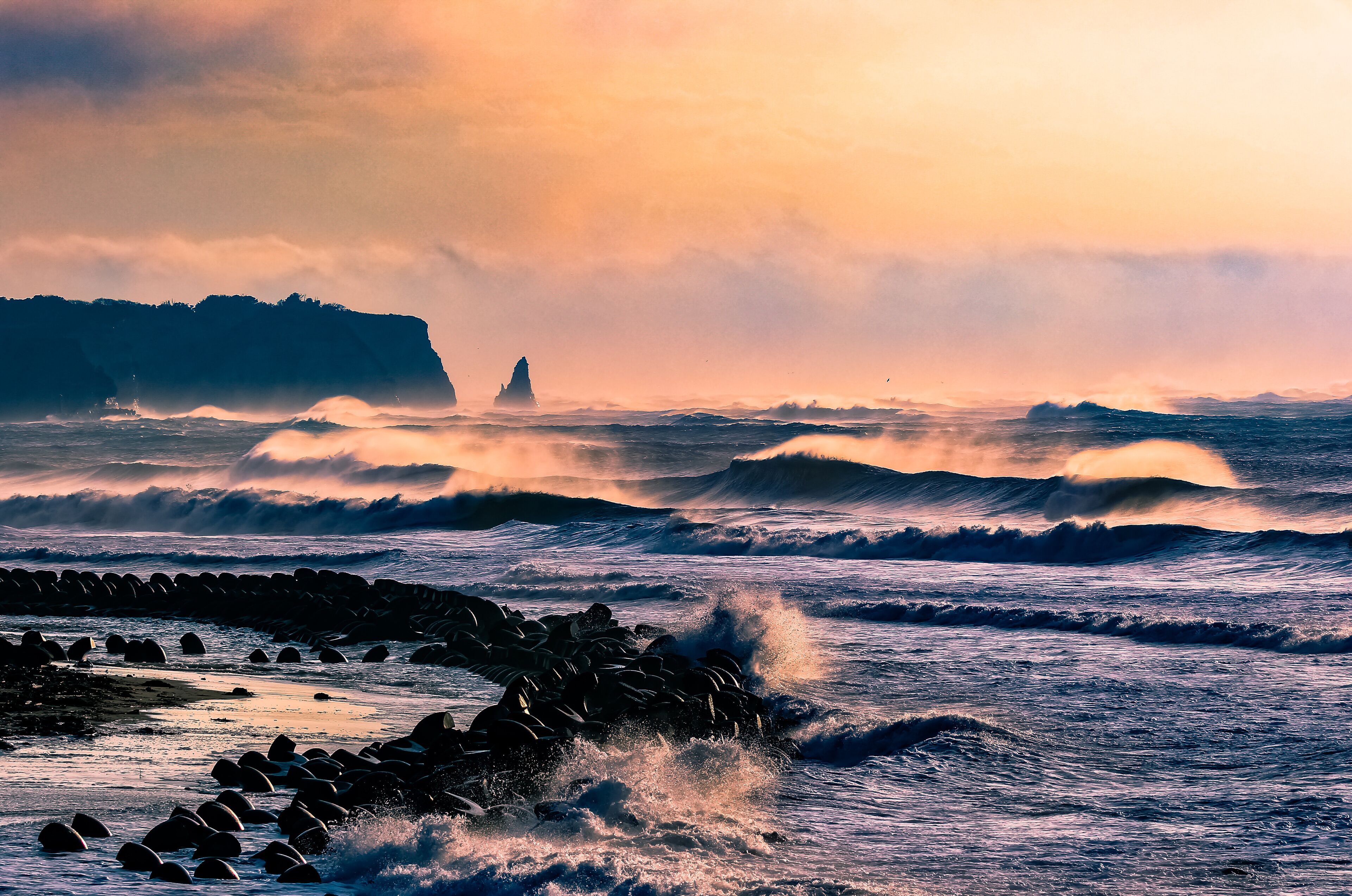 A rocky coastline with waves crashing against the shore and a lighthouse in the distance.