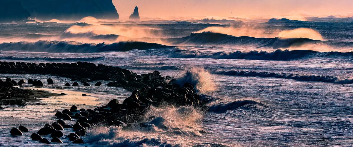 A rocky coastline with waves crashing against the shore and a lighthouse in the distance.