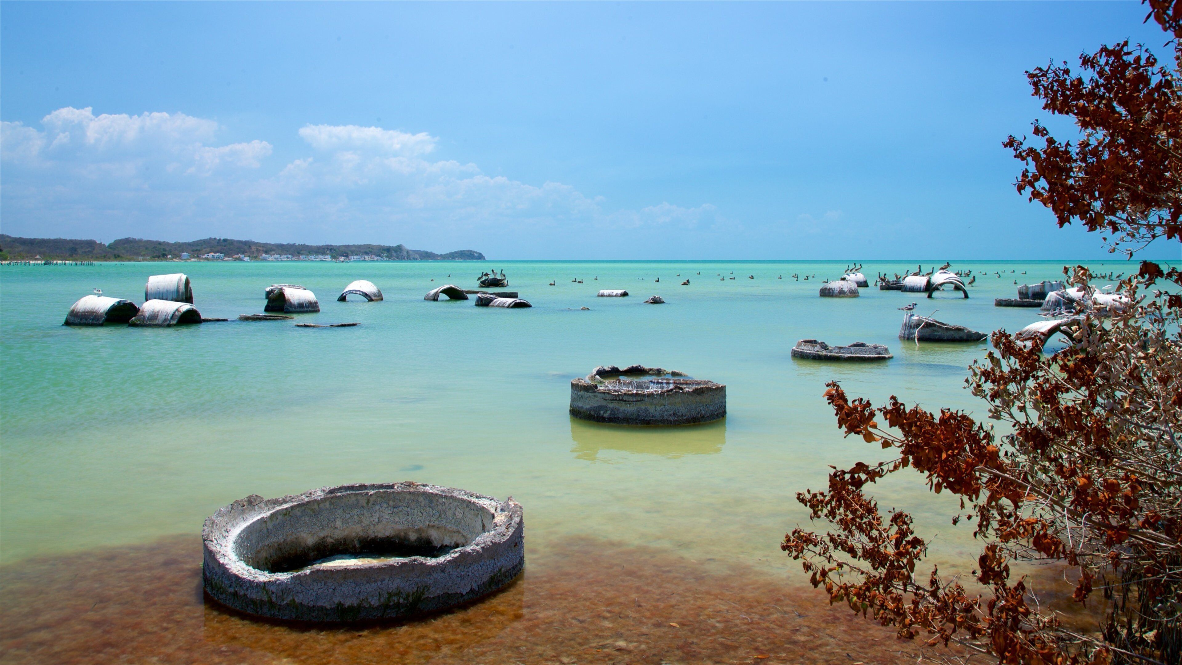 A coastal scene with clear turquoise water, large rocks, and a distant shoreline.