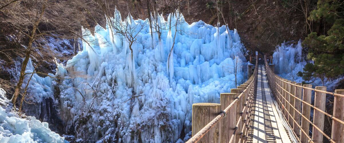 A wooden suspension bridge over a frozen river with icicles hanging from the surrounding trees.