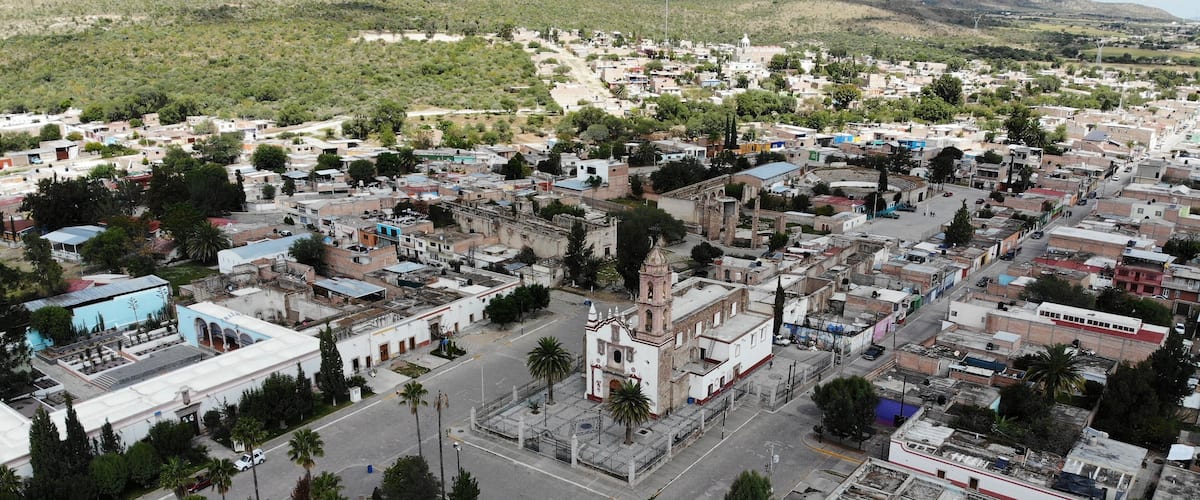 An aerial view of a town with a prominent church, a central plaza, and surrounding residential areas.