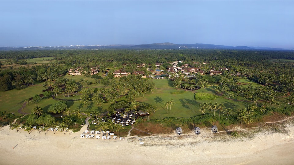 An aerial view of a resort with beachfront villas, a golf course, and surrounding tropical vegetation.