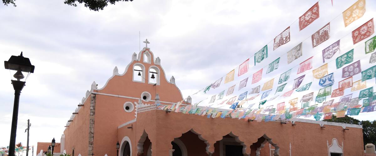 A pink building with arches and a bell tower, decorated with colorful flags.