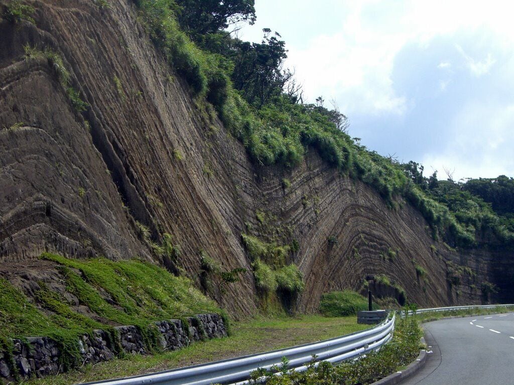 Volcanic ash-fall layers on Izu Oshima volcano in Japan. The volcanic ash was erupted into the air by the volcano. The ash then fell back onto ground. The ash was deposited during Pleistocene and Holocene times on an uneven ground surface. The ash layers are parallel to the curvature of the underlying ground surface. The folds are known as drape folds. The ash layers have not been folded after deposition..