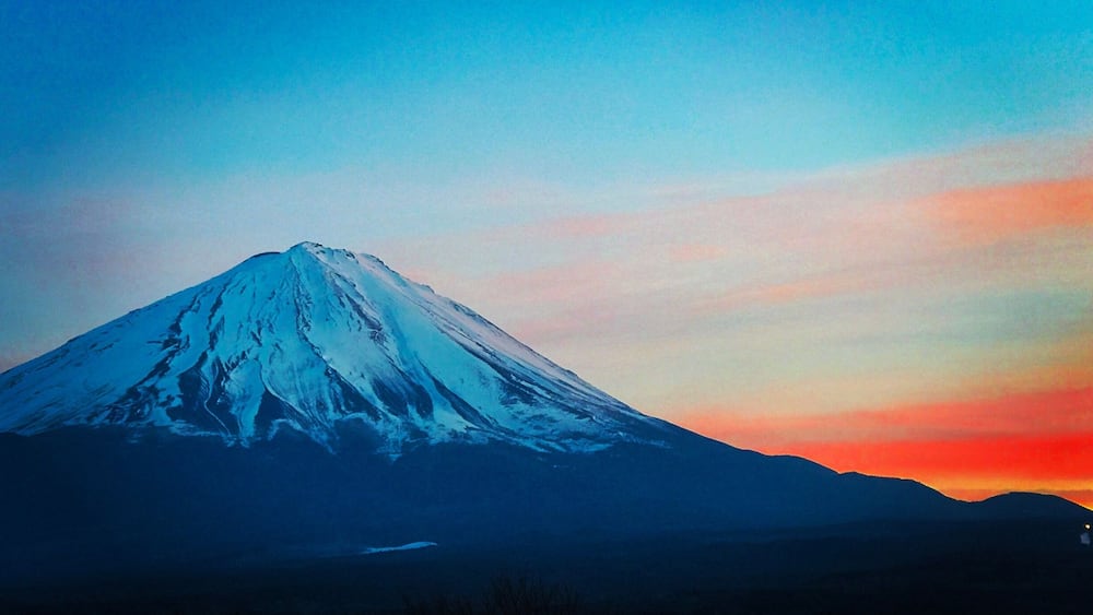A snow-capped mountain at sunset with a clear sky.