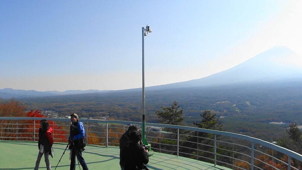 Eine Berglandschaft mit einem markanten Vulkan in der Ferne, umgeben von Bäumen in Herbstfarben und einem klaren Himmel.