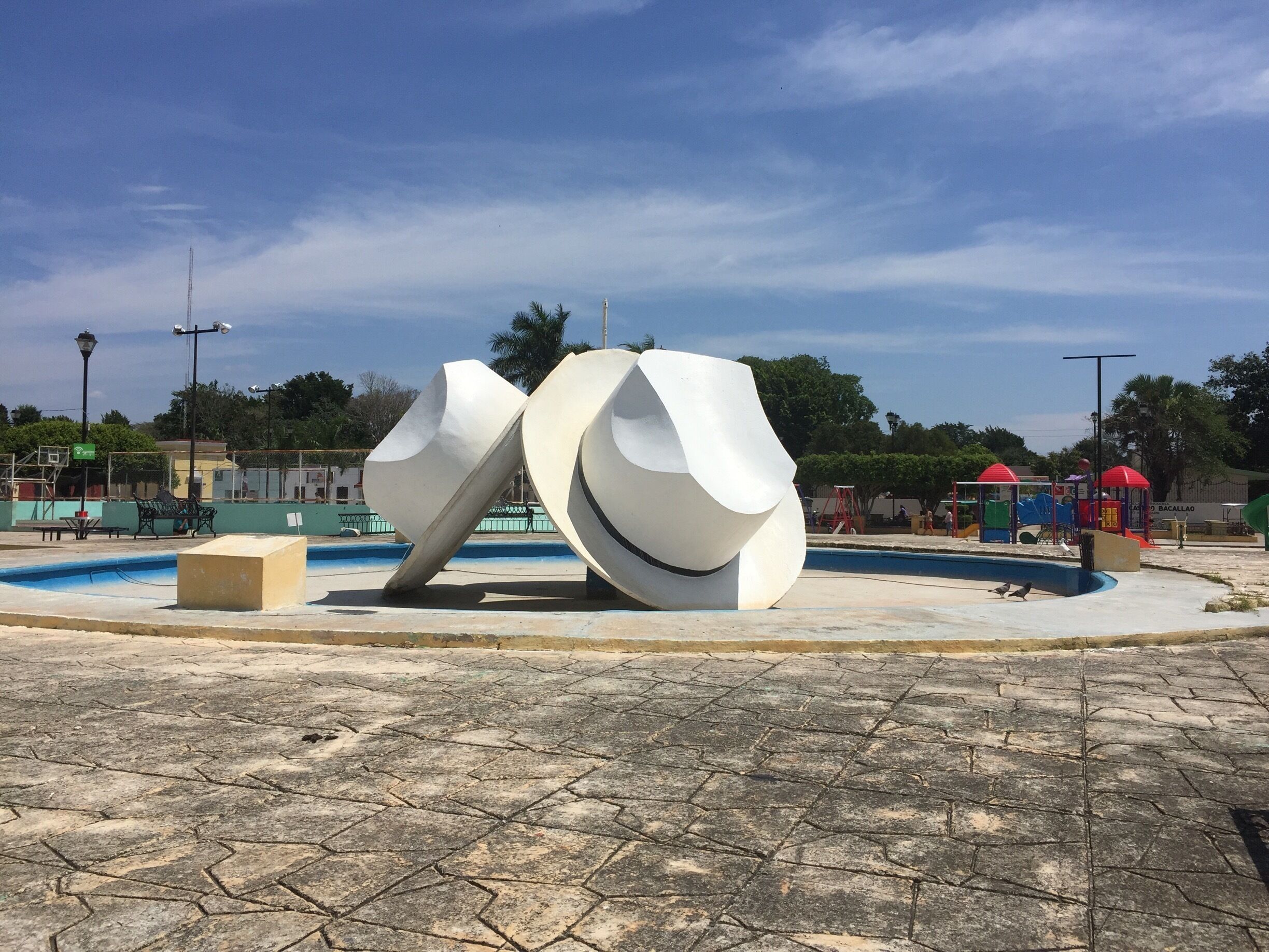 A modern sculpture in a public square with a pool and playground equipment.