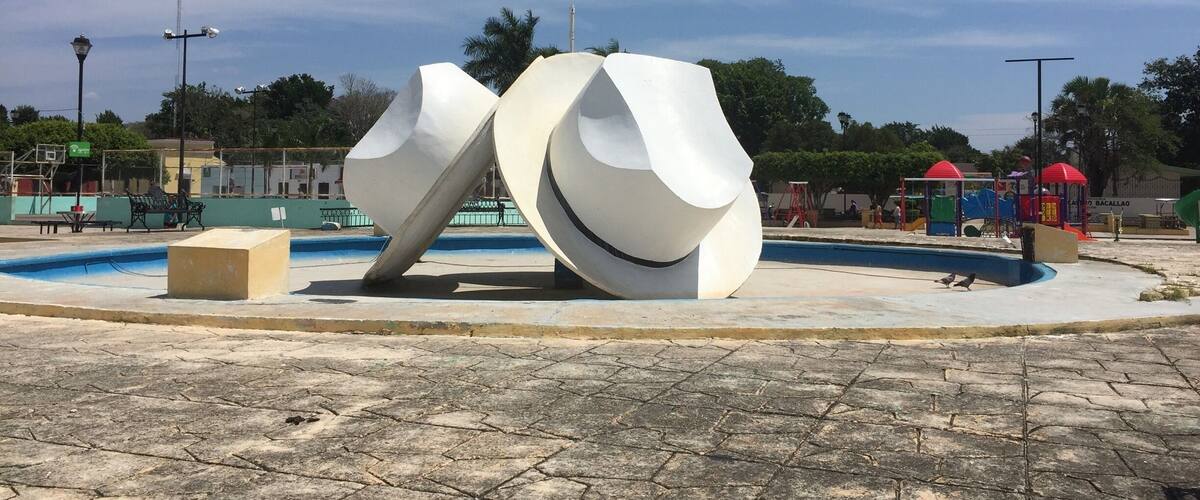 A modern sculpture in a public square with a pool and playground equipment.