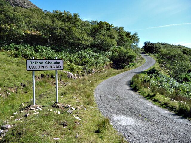 A winding road named Rathad Chaluim CALUM'S ROAD, surrounded by lush greenery and rocky terrain.