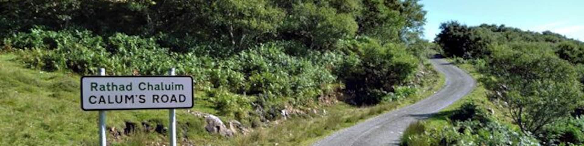 A winding road named Rathad Chaluim CALUM'S ROAD, surrounded by lush greenery and rocky terrain.