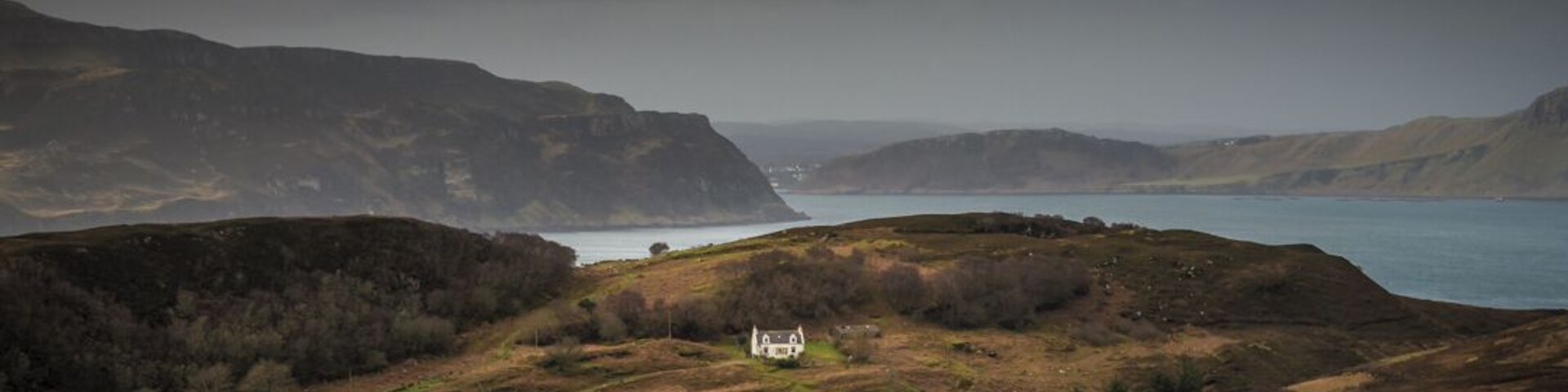 Una casa blanca en un valle con un lago y montañas al fondo.