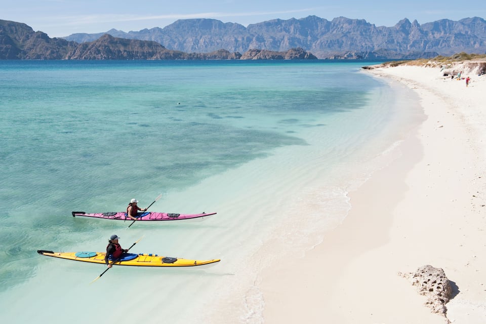 Una playa con kayak y montañas al fondo.