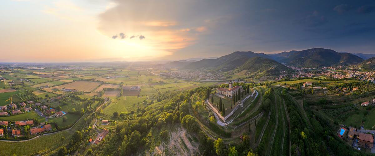 A panoramic view of a rural landscape with rolling hills, a fortified structure, and a small town nestled among fields.