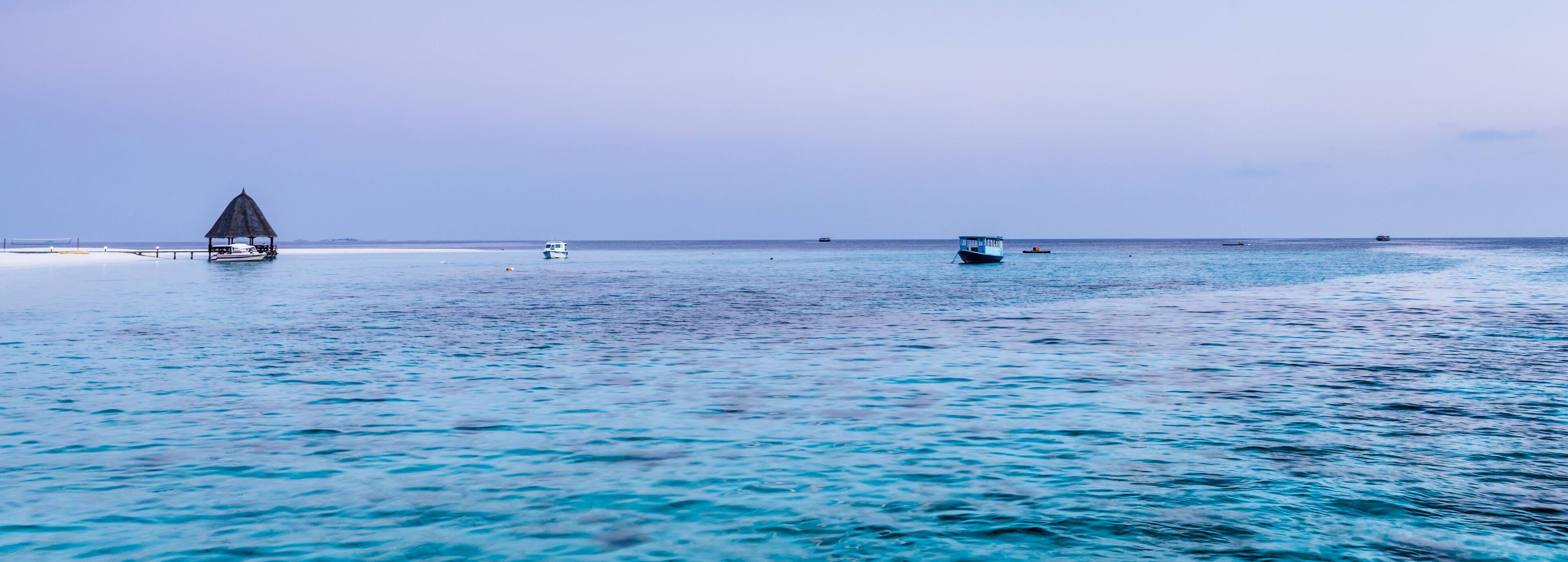 A calm sea with a small boat and a hut on a sandy beach.
