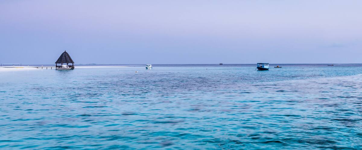 A calm sea with a small boat and a hut on a sandy beach.