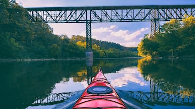 A red kayak on calm water with a bridge in the background.