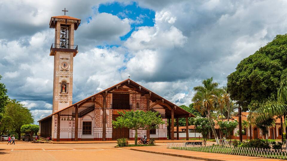 A church with a bell tower and a large tree in front.